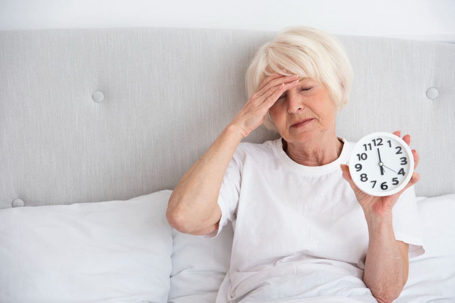 donna anziana stanca a letto con la sveglia in mano