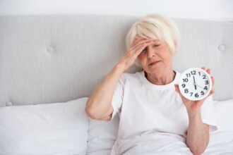 donna anziana stanca a letto con la sveglia in mano