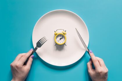 Mani che tengono coltello e forchetta su un piatto con una sveglia gialla